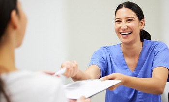 Woman in blue scrubs handing paperwork with clipboard to patients