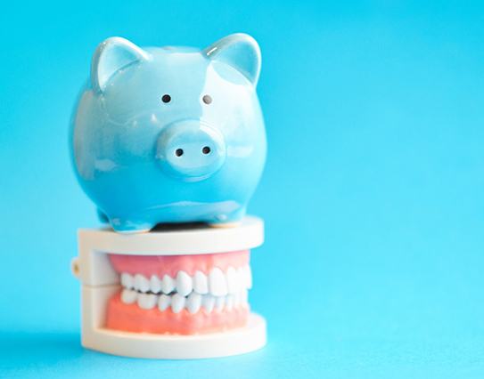 Piggy bank atop model teeth representing cost of cosmetic dentistry in Little Rock 