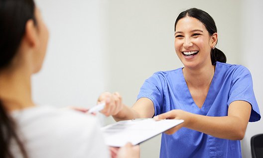 a front desk staff member handing a patient forms and a pen