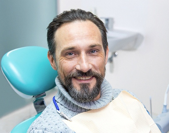 Man with beard smiling while sitting in dental chair