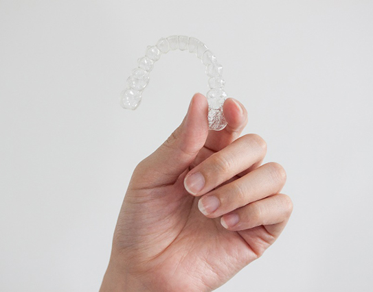 Patient holding up clear aligners against light grey background