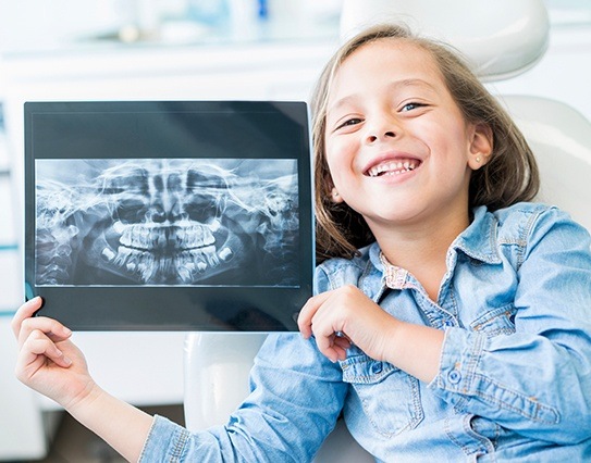 Young girl holding up x-rays during children's dentistry appointment