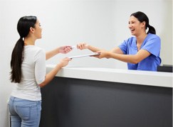 Dental receptionist smiling at patient while handing them forms