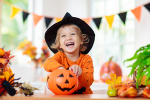 Child in witch’s hat reaching into a bucket for Halloween candy