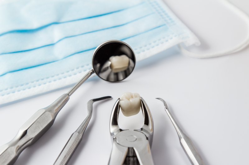 Forceps holding an extracted tooth near dental tools