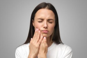 Woman touching one side of her jaw, wearing pained expression 