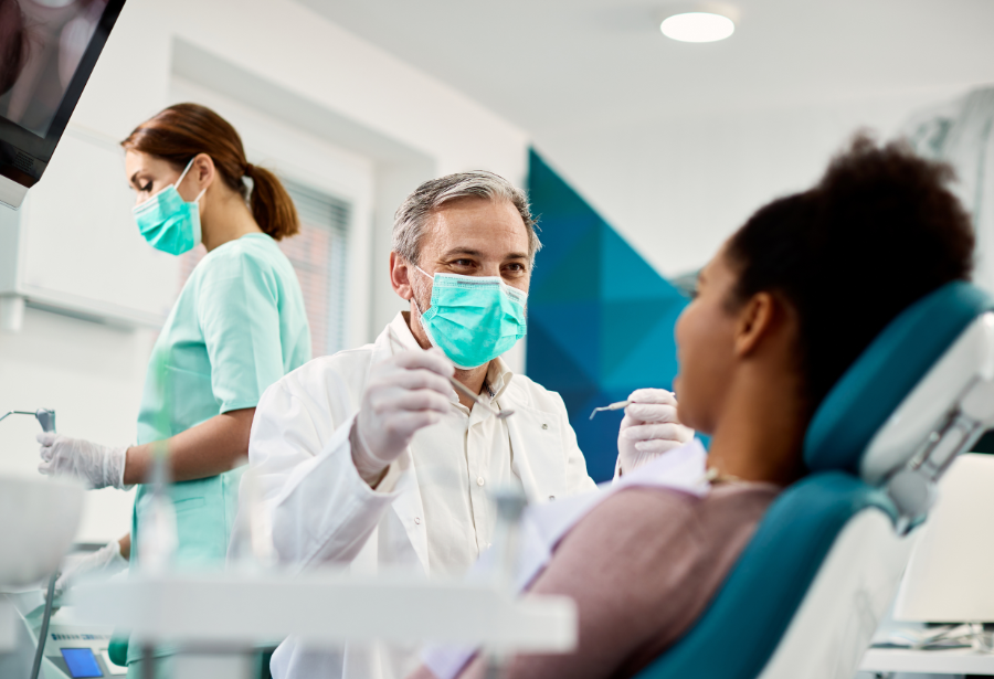 Patient in dental chair with dentist wearing mask and holding instruments